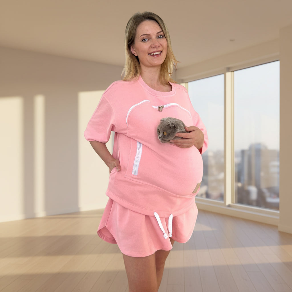 Woman wearing a pink outfit with a pouch, holding a small animal against a white background Main image
