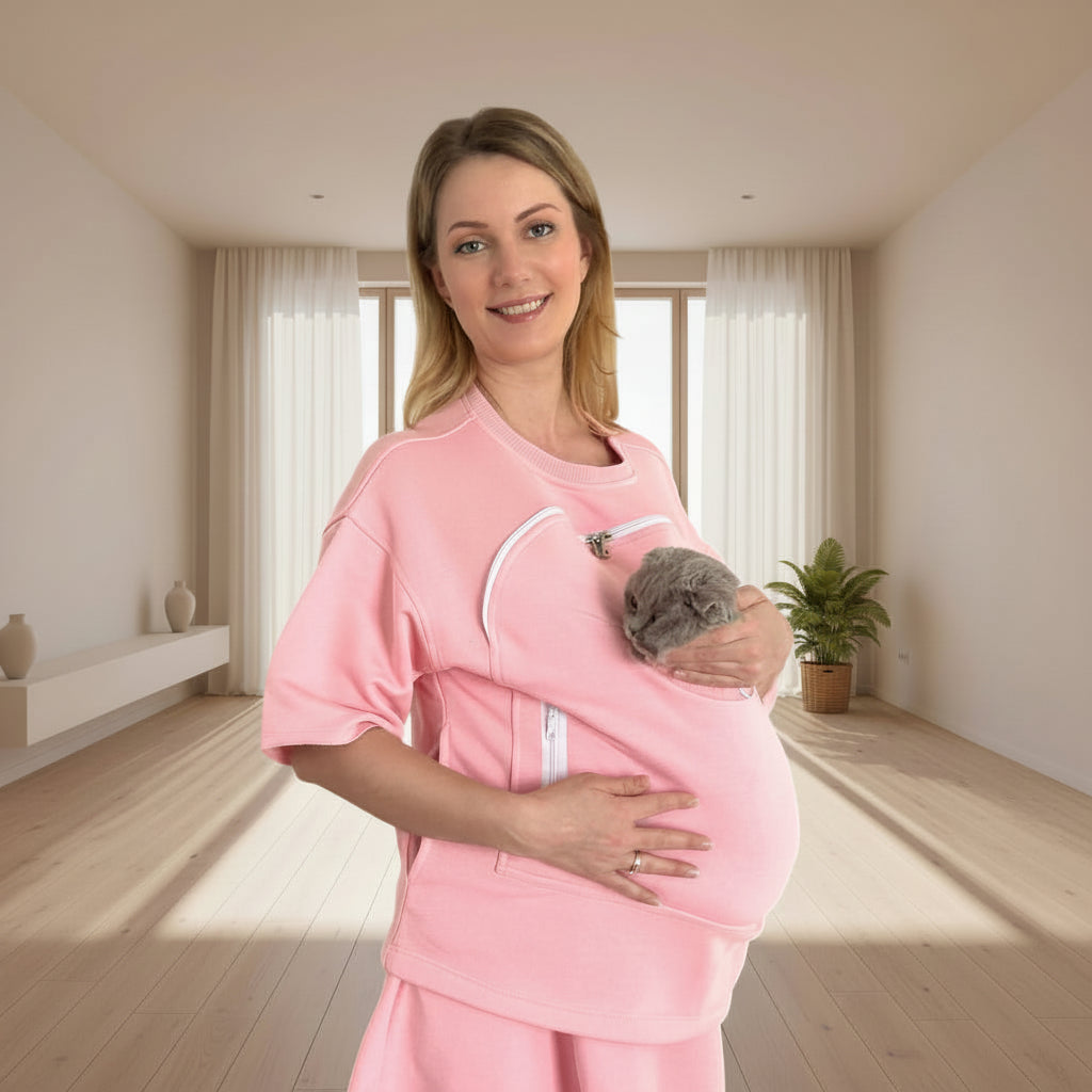 Woman wearing a pink carrier holding a cat in a bright room.