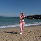 Person in a pink outfit taking a selfie on a beach with ocean and sky in the background