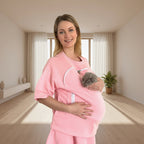 Woman wearing a pink pet carrier holding a cat in a bright room.