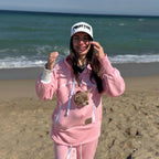 Person in pink hoodie with dog in pocket on beach