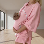 Person wearing a pink outfit with a pet carrier holding in a minimalistic room.