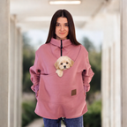 Women wearing a pink sweatshirt with a dog in the pocket, standing indoors.