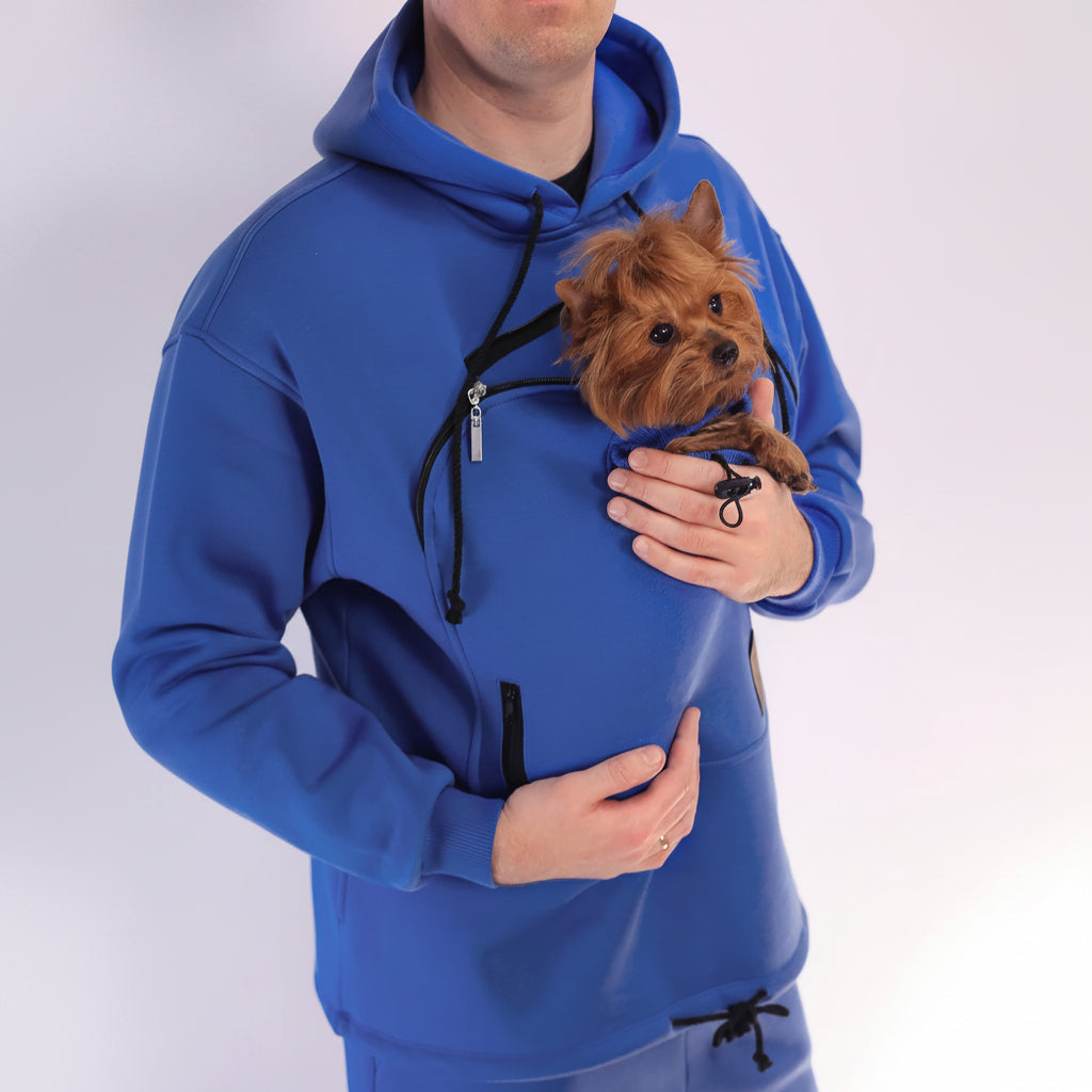 Men wearing a royal blue hoodie with a front pocket holding a small brown dog.