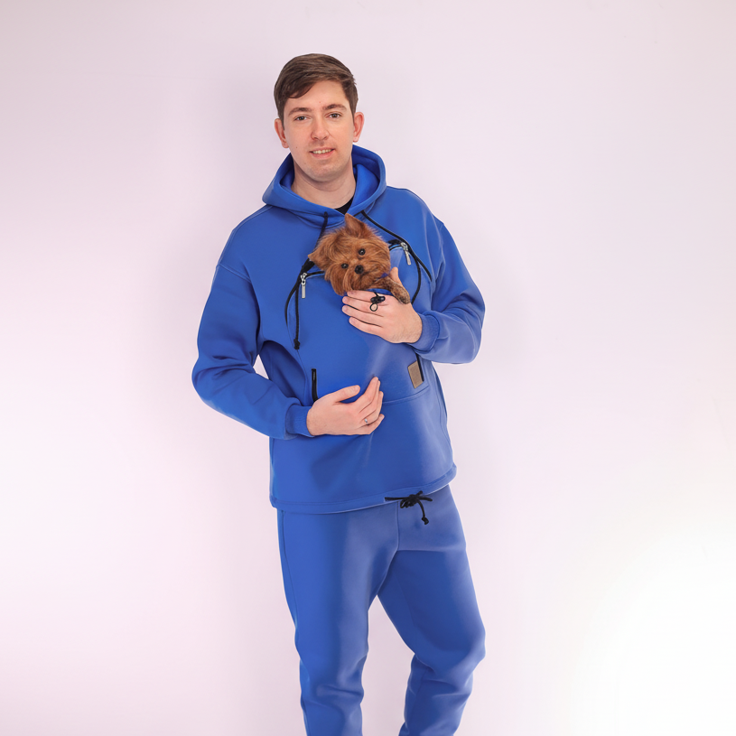 Man wearing a royal blue tracksuit holding a small dog on a white background Main image