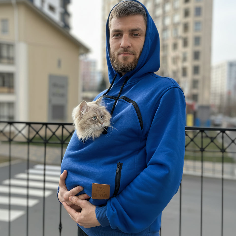 Man wearing a royal blue hoodie with a cat in a pouch, standing outdoors.