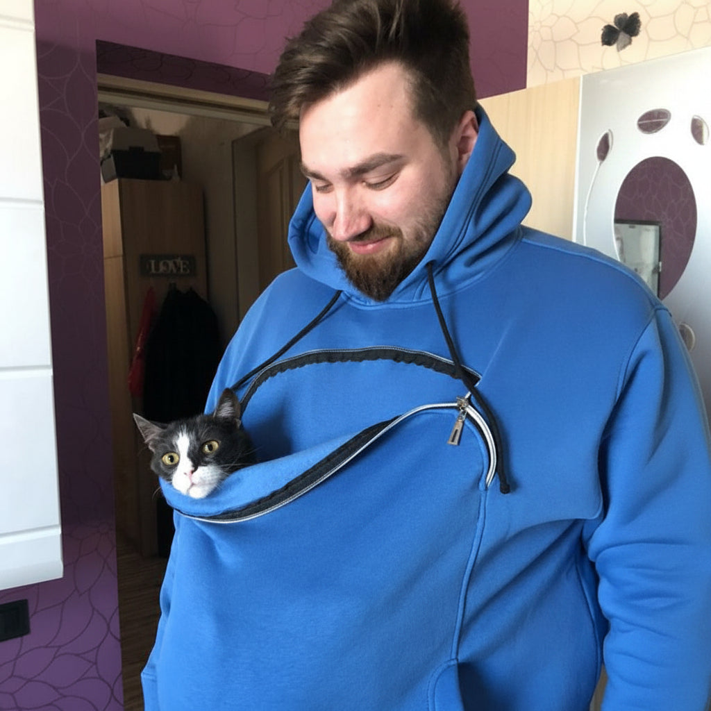 Man wearing a royal blue hoodie with a cat in a pouch, standing in a room.