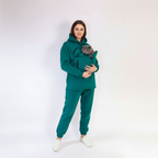 Person wearing a green teal tracksuit holding a gray cat on a white background