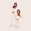 Two people in matching white set holding small dogs on a plain background