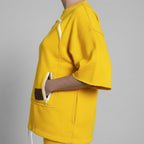 Person wearing a yellow outfit with a white zip in a room.
