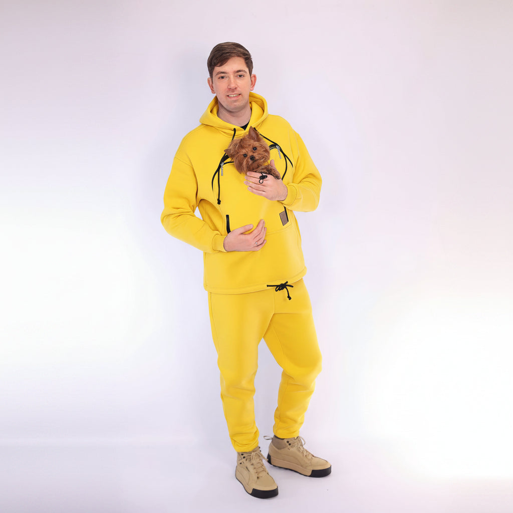 Person wearing a yellow hoodie and matching pants holding a small dog on a white background