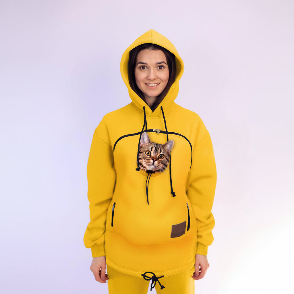 Person wearing a yellow hoodie with a cat peeking out of the pocket against a white background